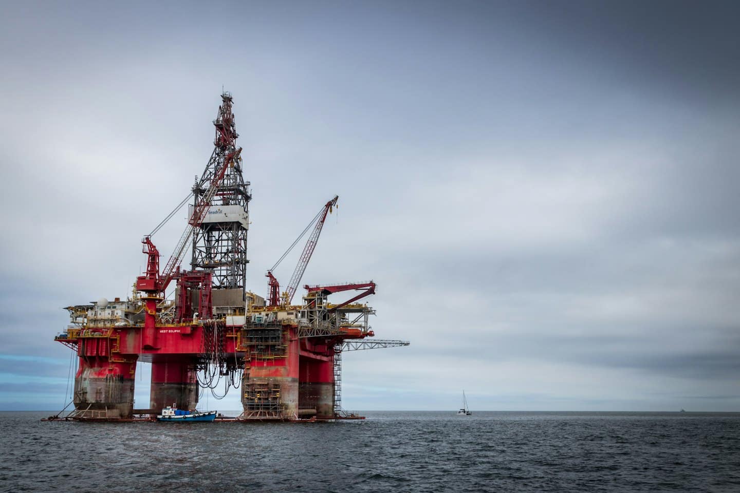Duża czerwono-szara platforma wiertnicza na oceanie z łodzią roboczą.